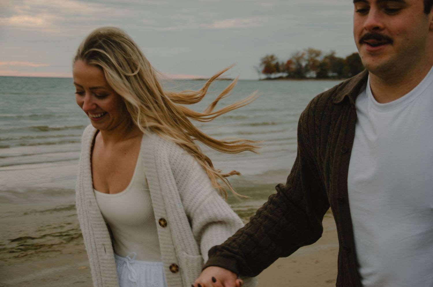 Two people in casual attire share a romantic moment on an overcast beach.