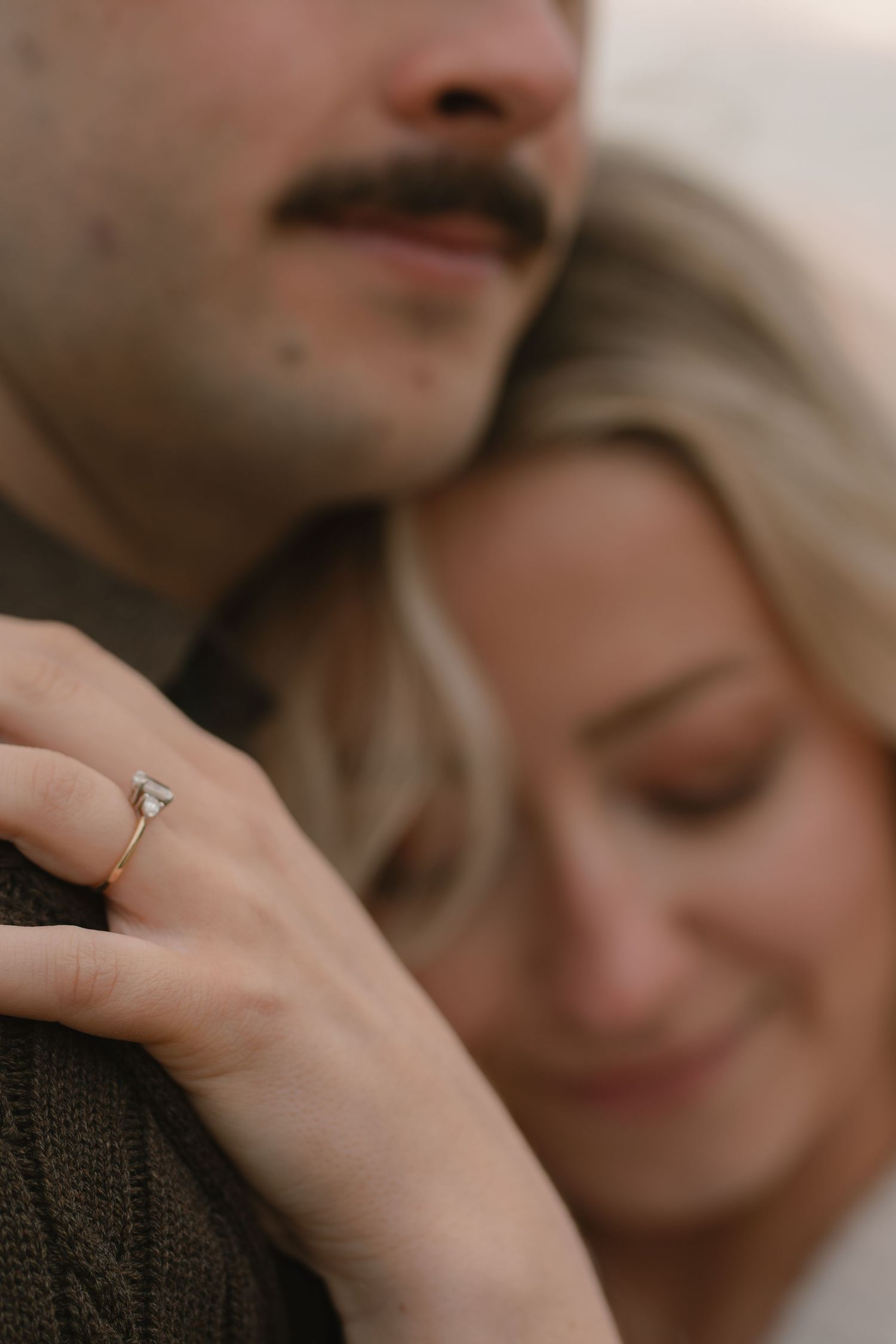 Close-up shots of a couple sharing intimate moments and showing off an engagement ring on the beach at sunset.