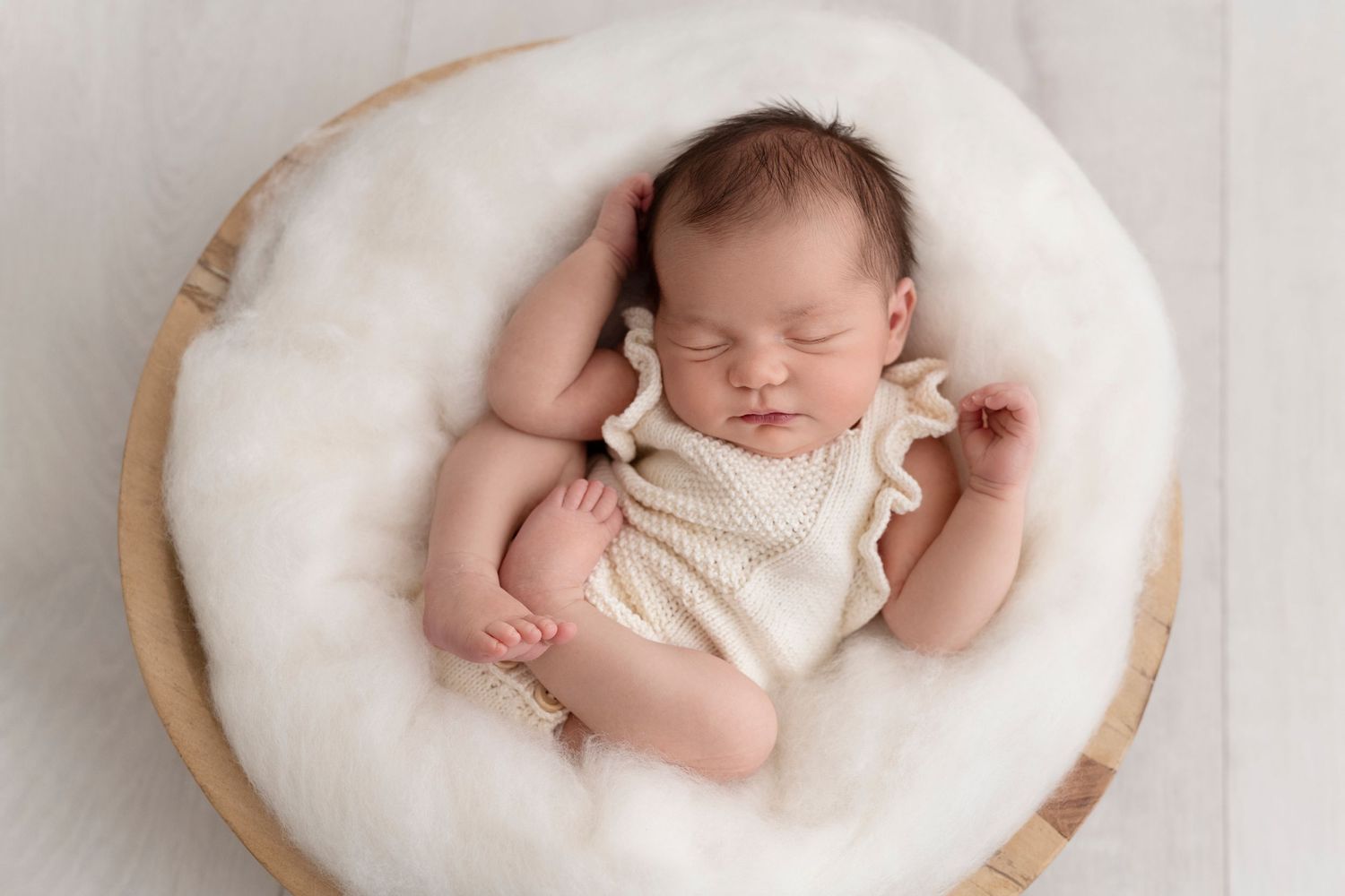 A sleeping newborn baby lies peacefully in a round white cushioned nest during a professional photo session.