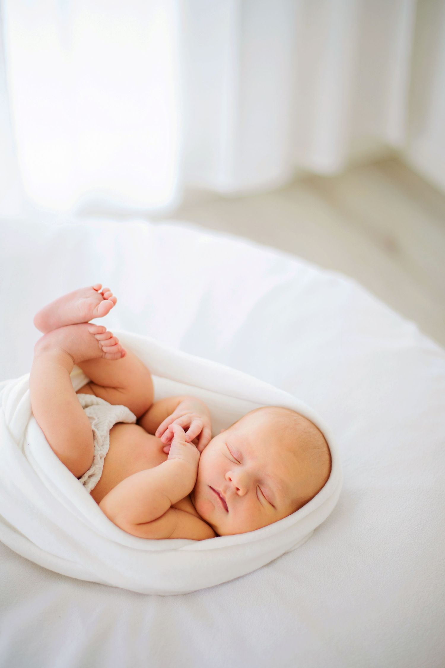 En sovande nyfödd baby insvept i mjukt vitt tyg ligger lugnt på en ljus yta.