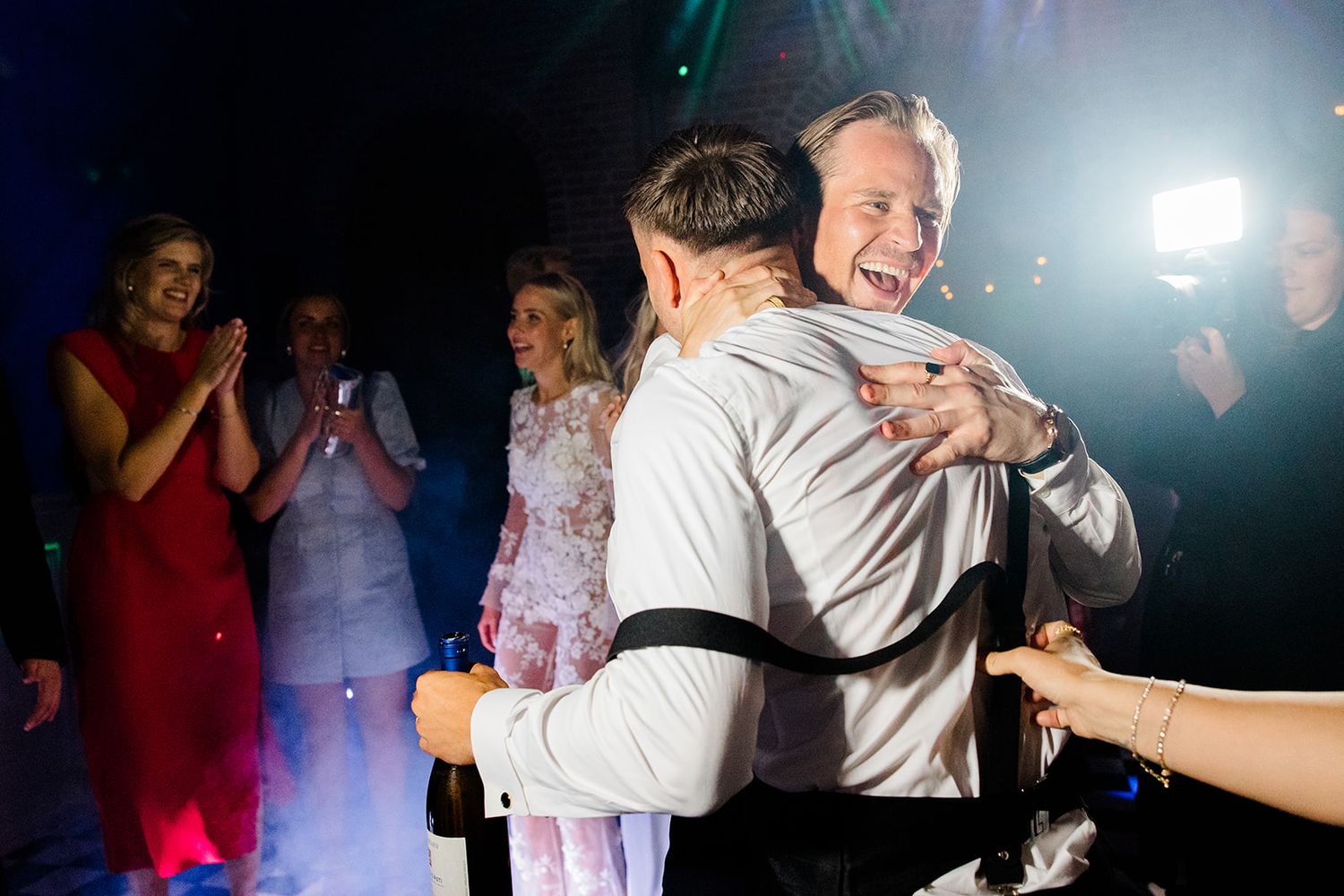 Couples dancing together at a dimly lit wedding reception with flashing lights and festive atmosphere.