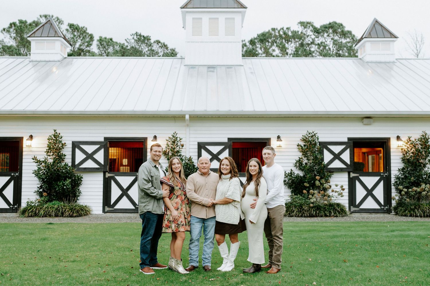 Family gathered in front of a white farmhouse-style building with black trim details.