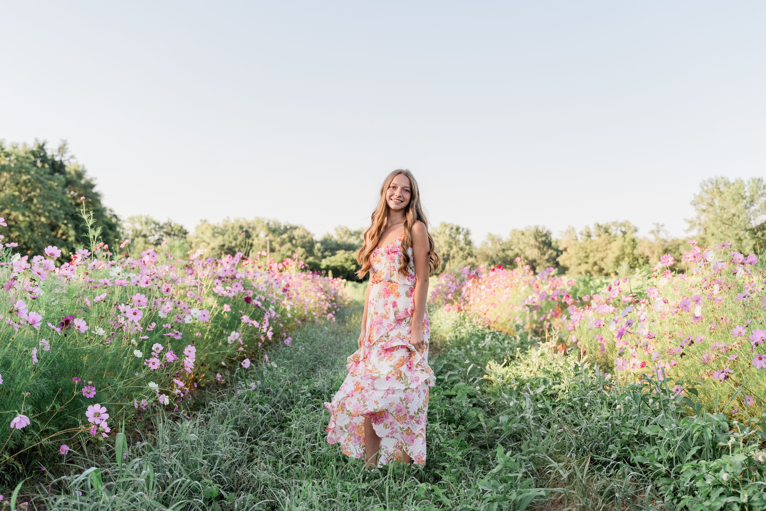 A person in a floral dress poses in a wildflower field during golden hour sunset.