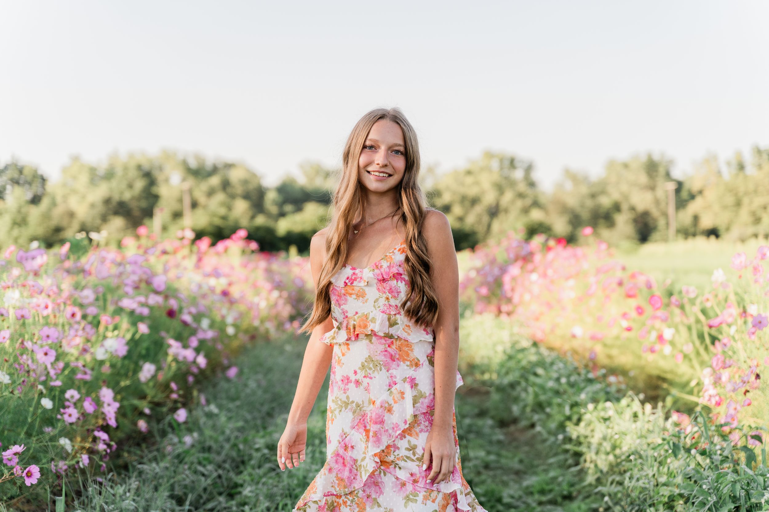 A woman in a floral dress stands in a blooming flower garden during golden hour.