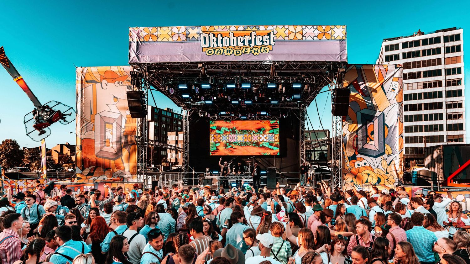 Crowded music festival with vibrant stage setup and colorful teal sky.
