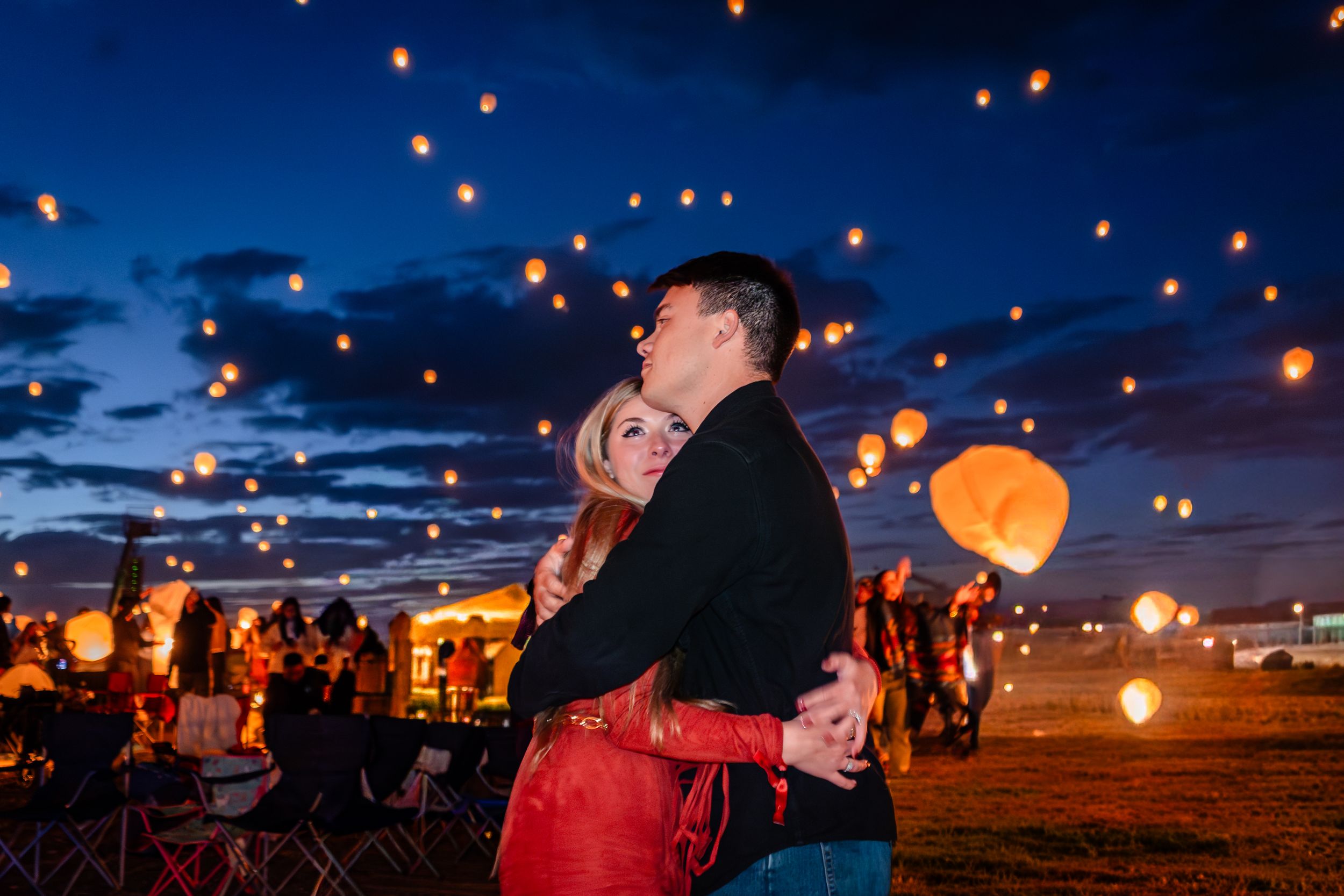 A group of people release glowing paper lanterns into the dark night sky at a festival celebration.