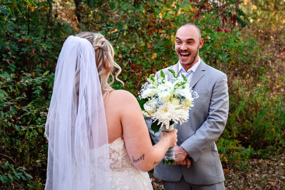 A joyful first look moment between bride and groom outdoors with white bouquet and grey suit.