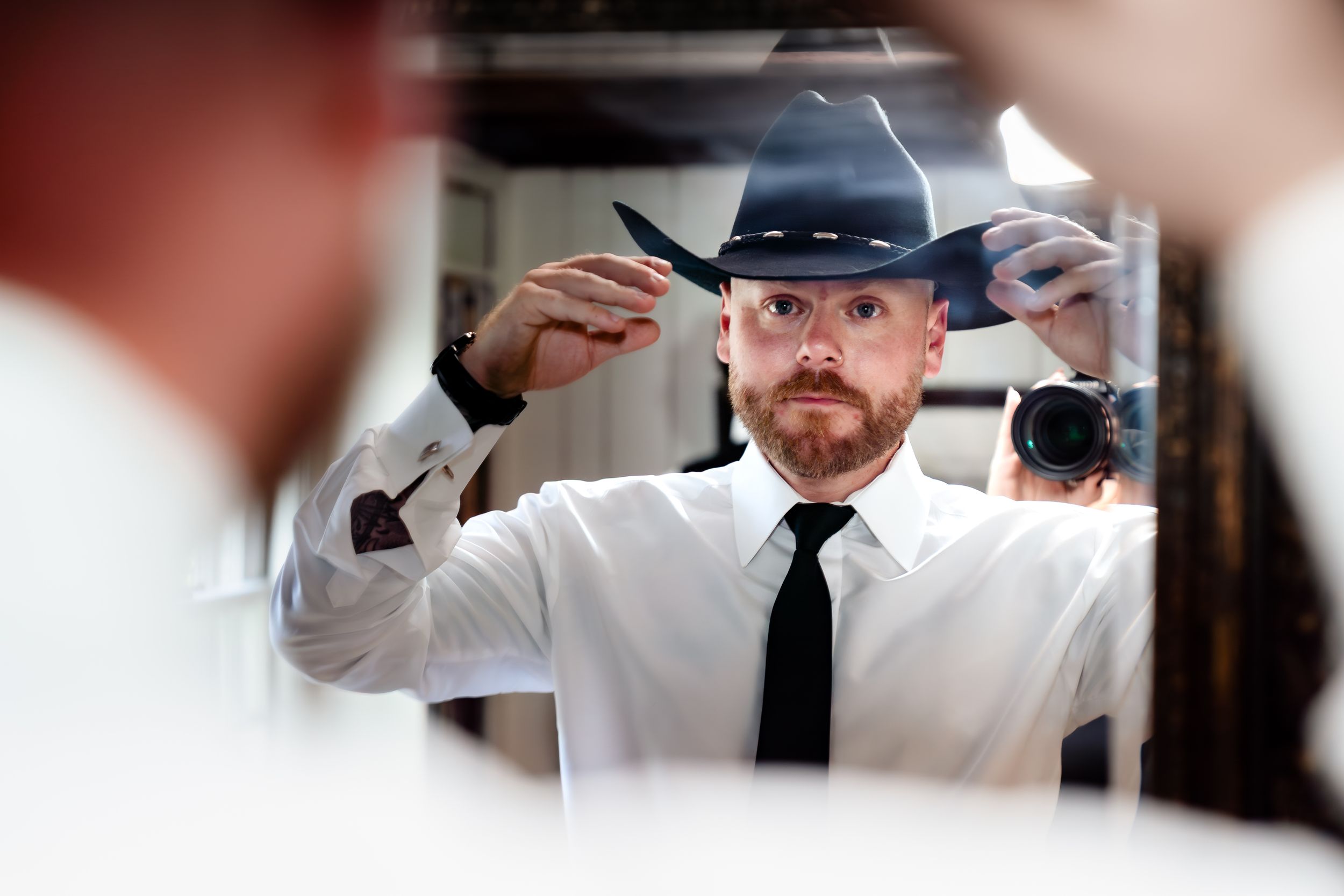 A person in a white shirt and black hat pours a cocktail into a glass at a bar.