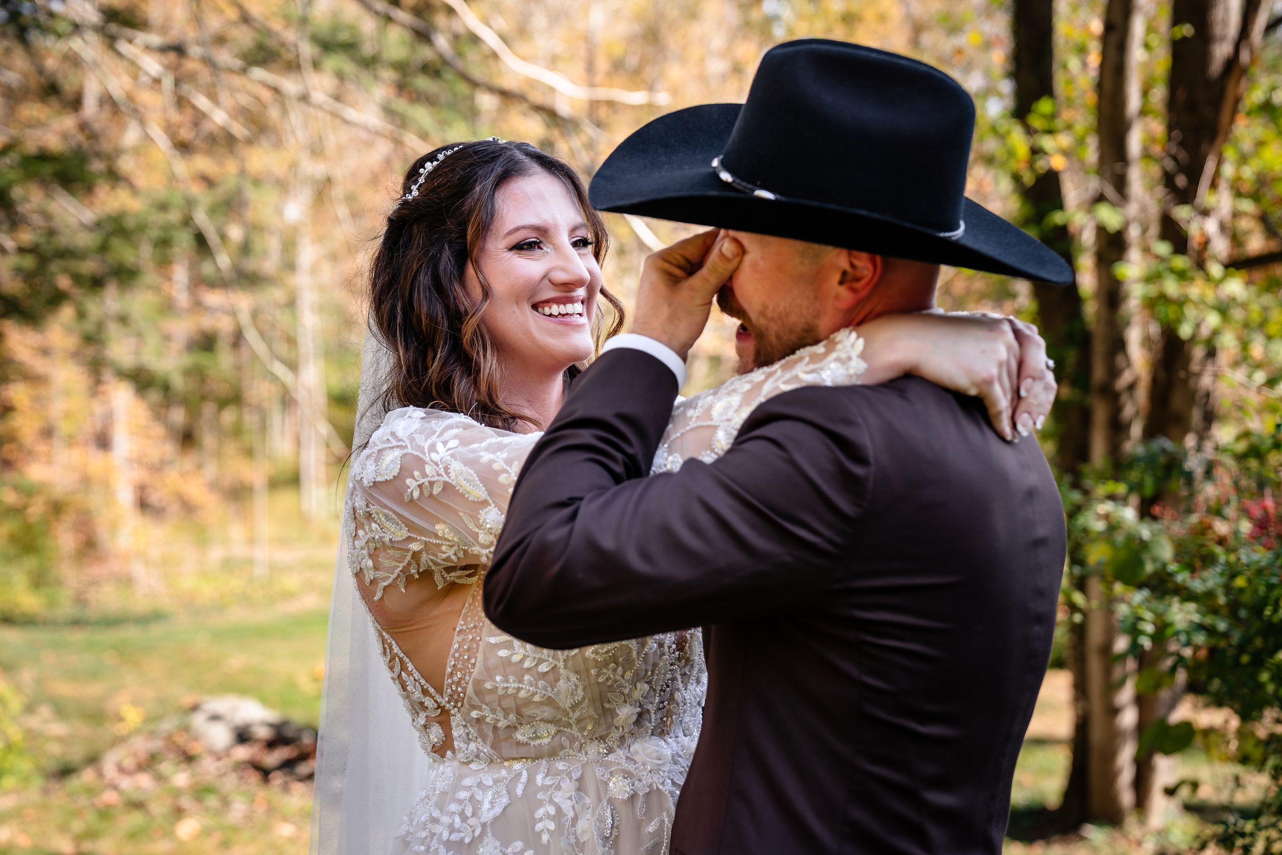 A couple in wedding attire dances and embraces outdoors surrounded by autumn trees and foliage.