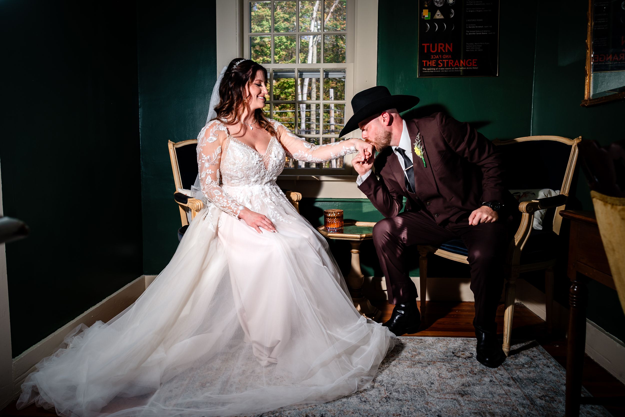 Bride in a flowing white dress lounges on a vintage green couch while her partner kneels beside her in a romantic pose.