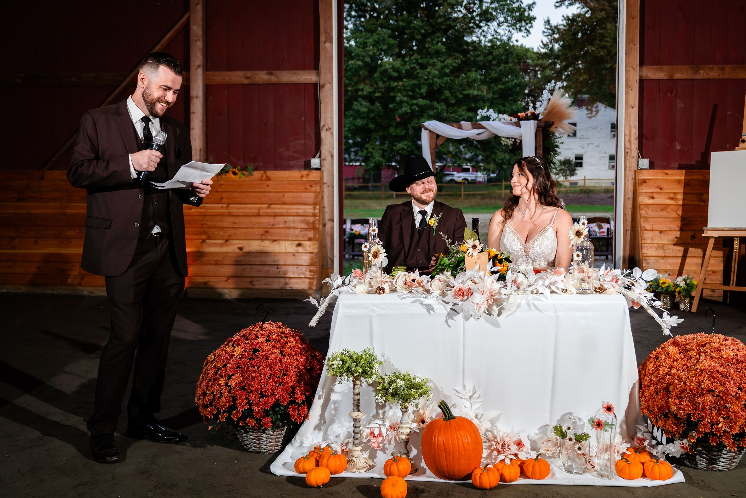 A rustic fall wedding reception setup with pumpkins and floral decorations on wooden tables at an autumn-themed venue.
