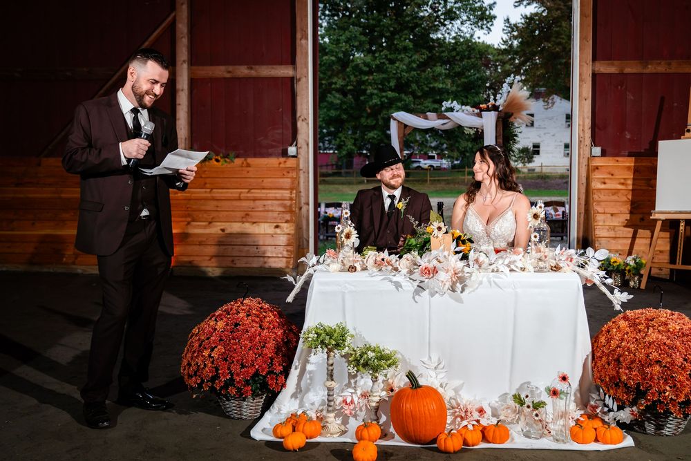 A rustic fall wedding reception setup with pumpkins and floral decorations on wooden tables at an autumn-themed venue.