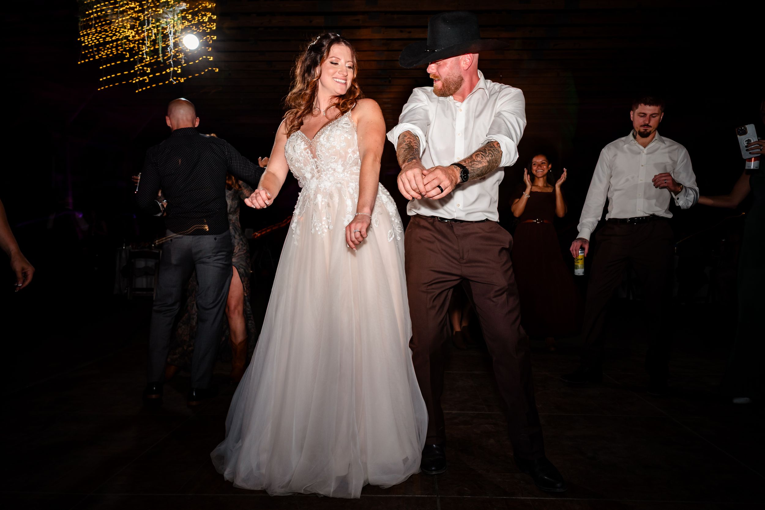 A couple dances together in a dimly lit venue with the bride wearing a flowing white wedding gown.