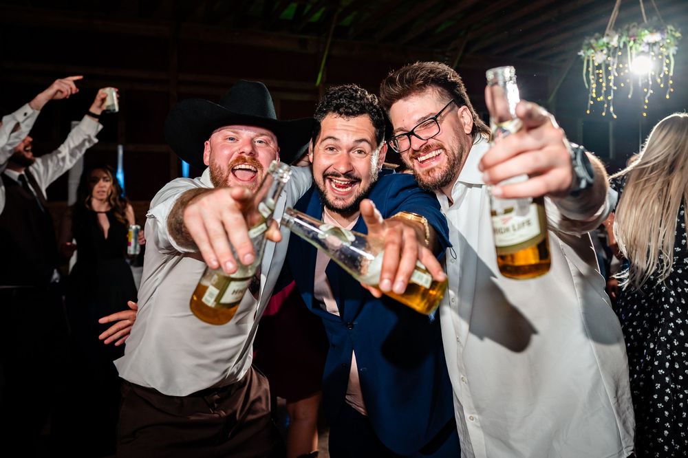 Party guests raise their beer bottles in celebration at a lively indoor event with dark lighting.