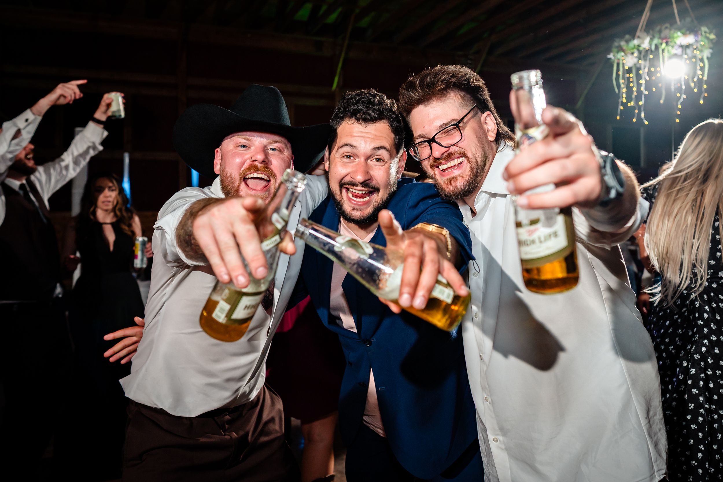 Party guests raise their beer bottles in celebration at a lively indoor event with dark lighting.