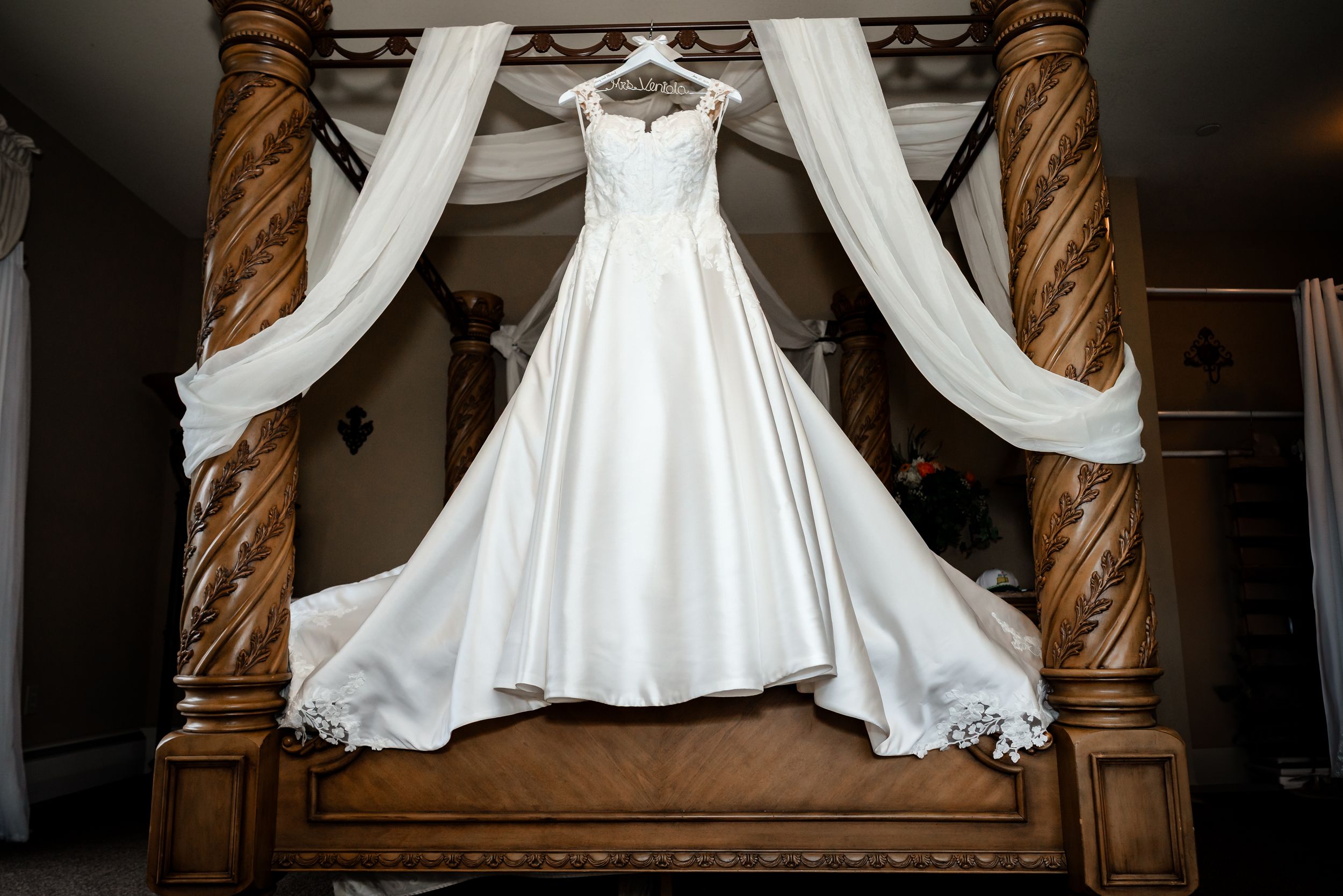 A collection of white wedding dresses displayed in a dimly lit room with ornate wooden columns and draping fabric.