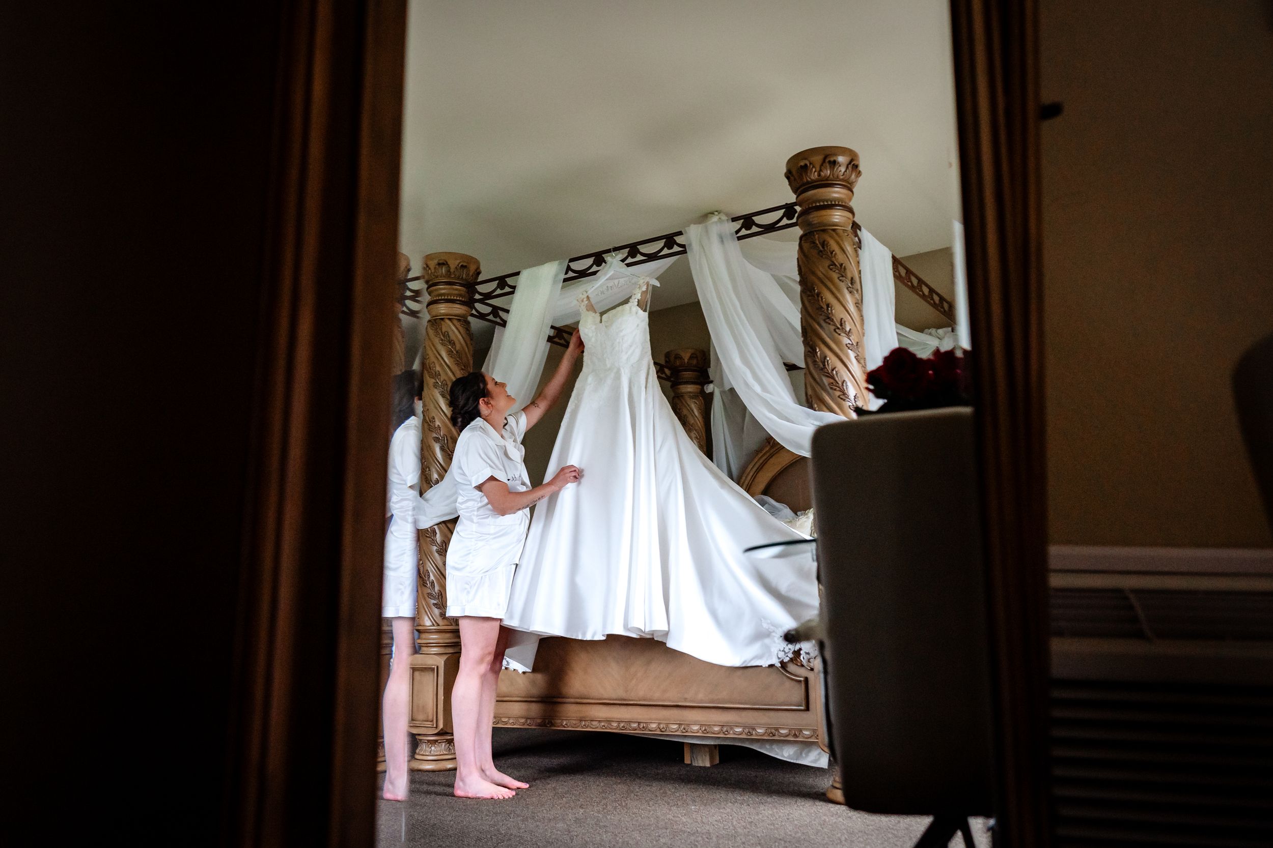 Wedding dress being buttoned up in preparation for the ceremony in a dimly lit room.