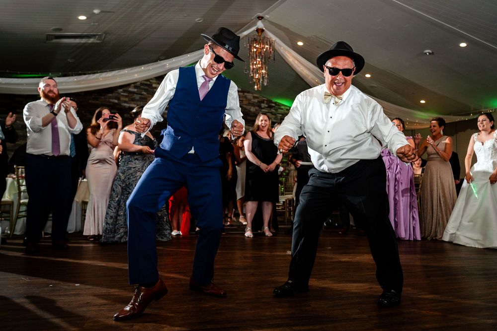 Wedding guests dancing and jumping energetically on a dark dance floor with ambient lighting.