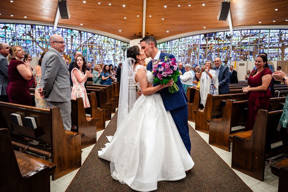 A wedding ceremony in a church with wooden pews and twinkling string lights overhead.