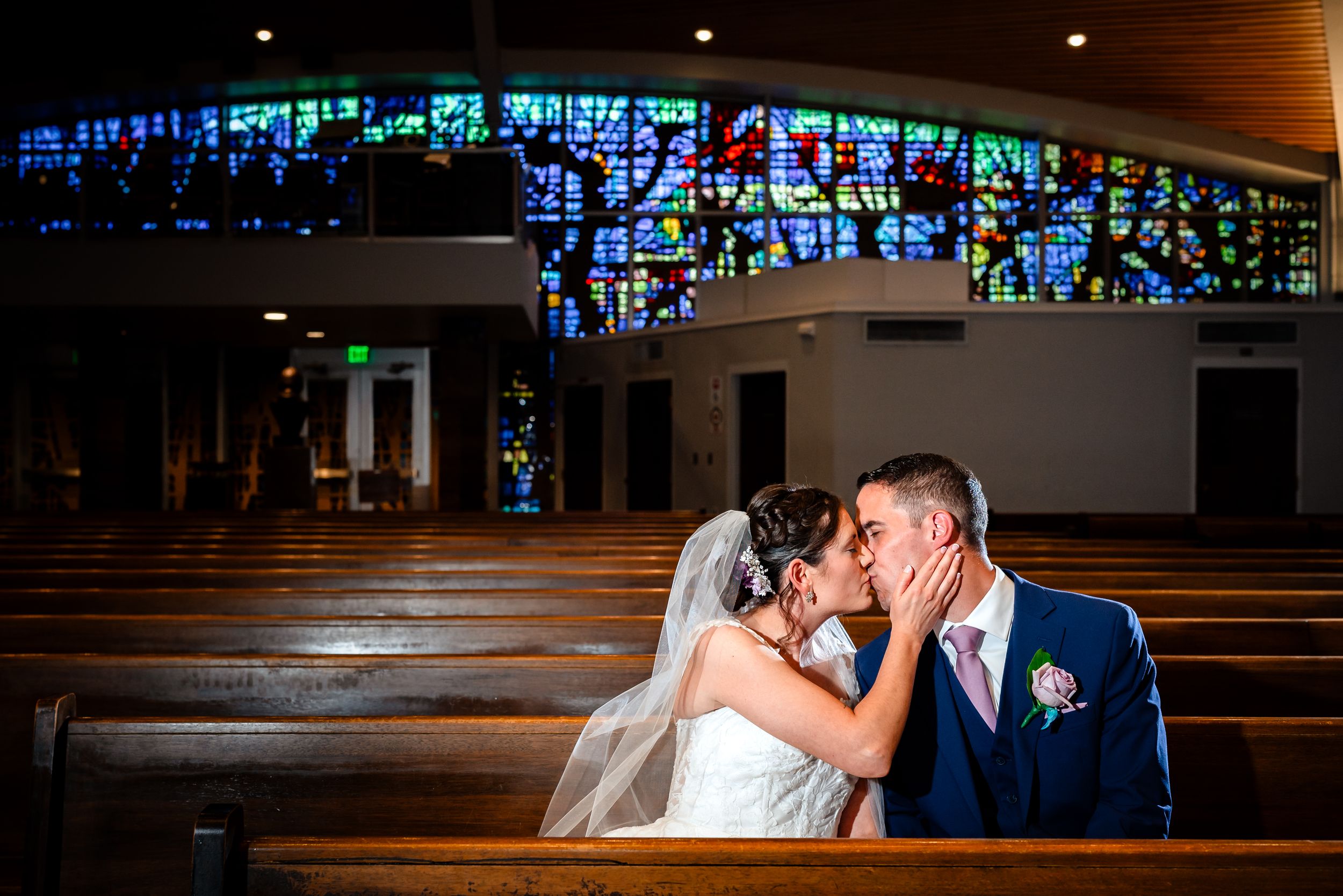 Newlyweds share an intimate moment inside a church with beautiful stained glass windows in the background.