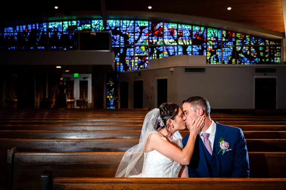 Newlyweds share an intimate moment inside a church with beautiful stained glass windows in the background.