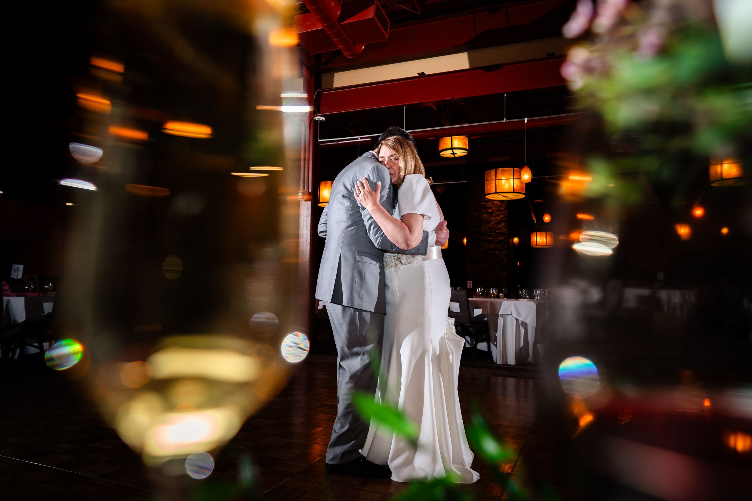 A couple in formal wedding attire share an intimate dance moment under warm lighting at an evening reception.