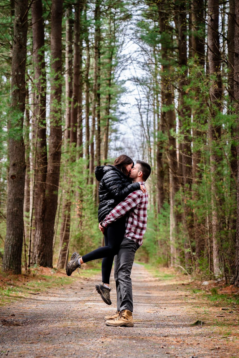 A couple shares a romantic kiss while hiking on a tree-lined forest trail during autumn.