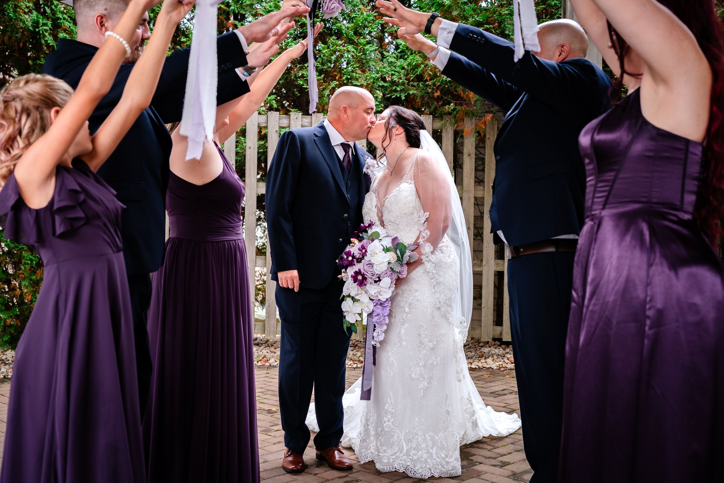 Wedding party celebrates with raised champagne glasses outdoors in a garden setting.