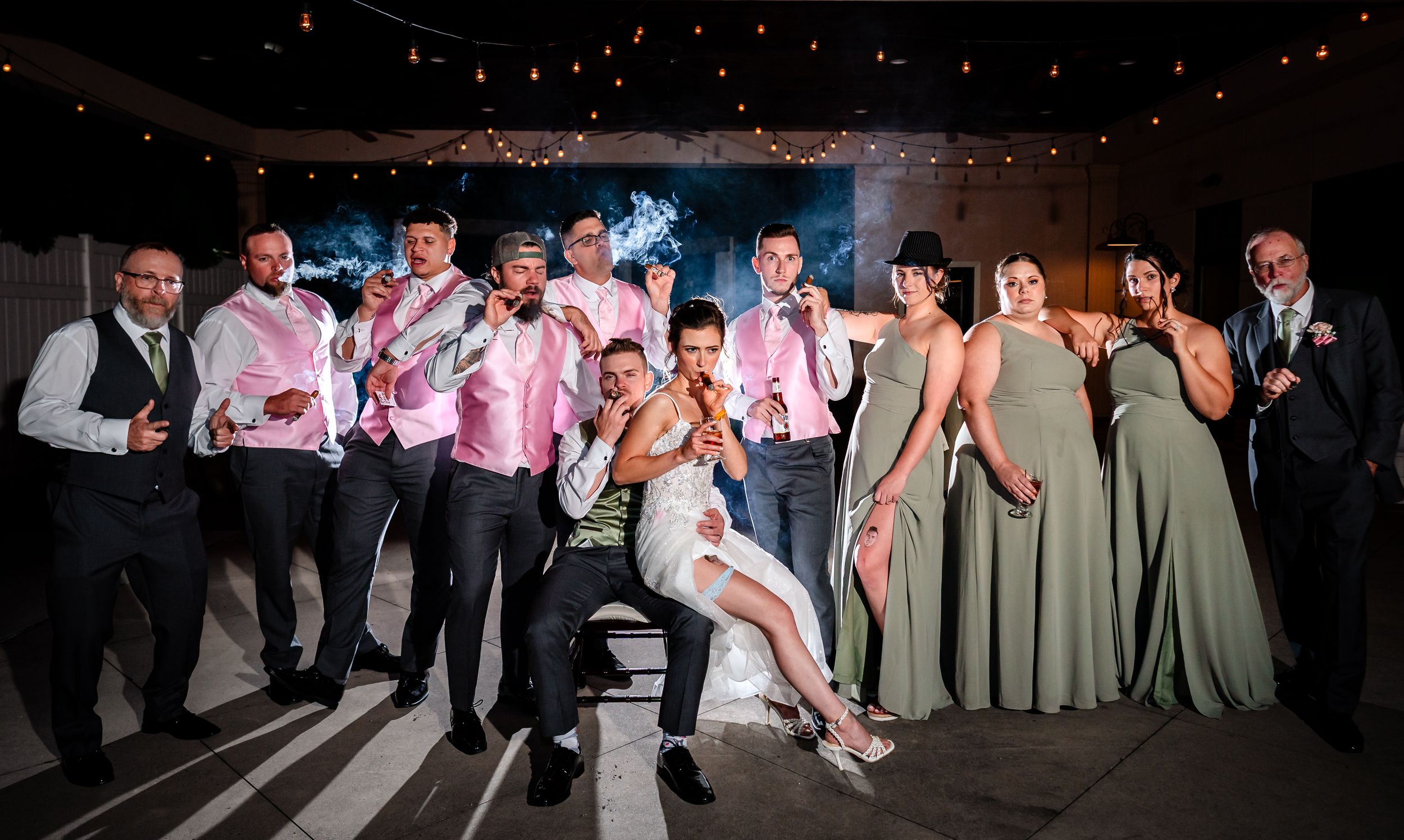 Wedding reception guests dance and celebrate on a dark dance floor illuminated by string lights above.