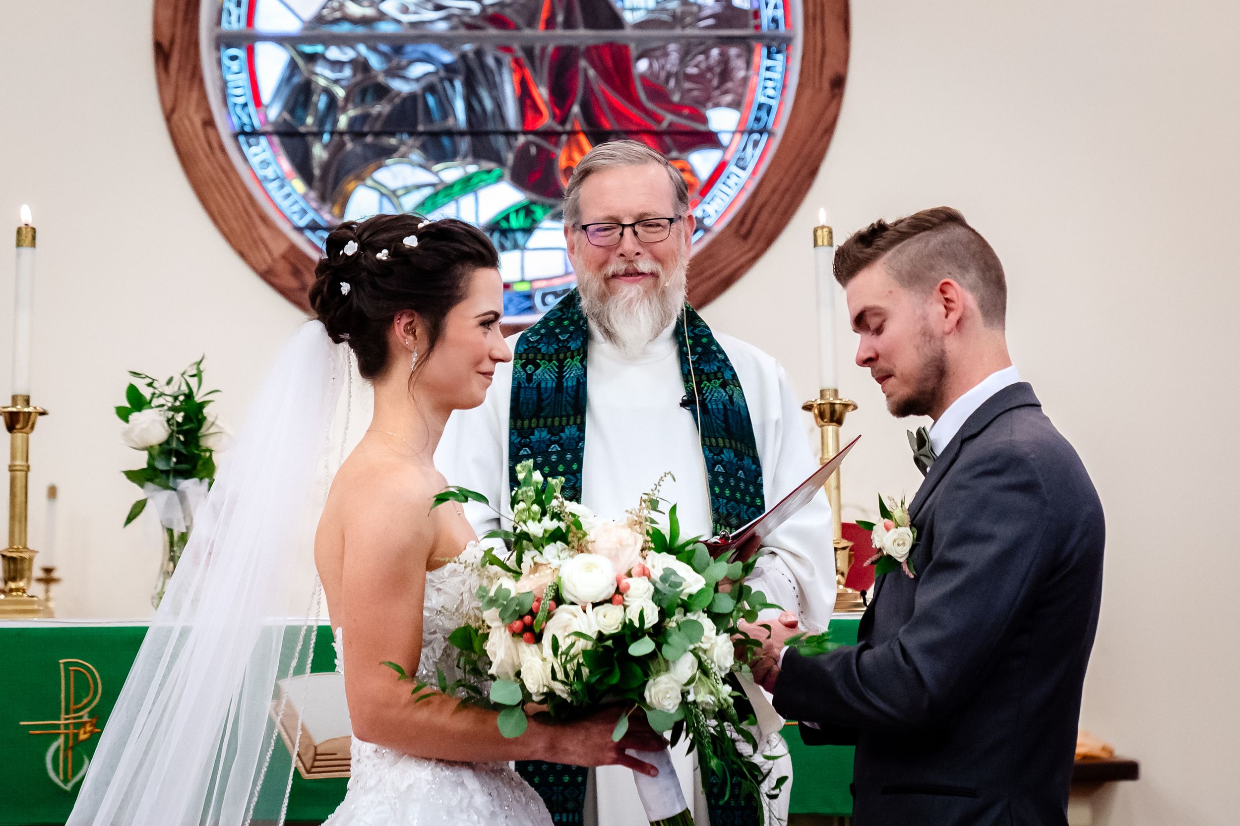 A couple shares an intimate moment during their wedding ceremony in front of a church altar with floral decorations.