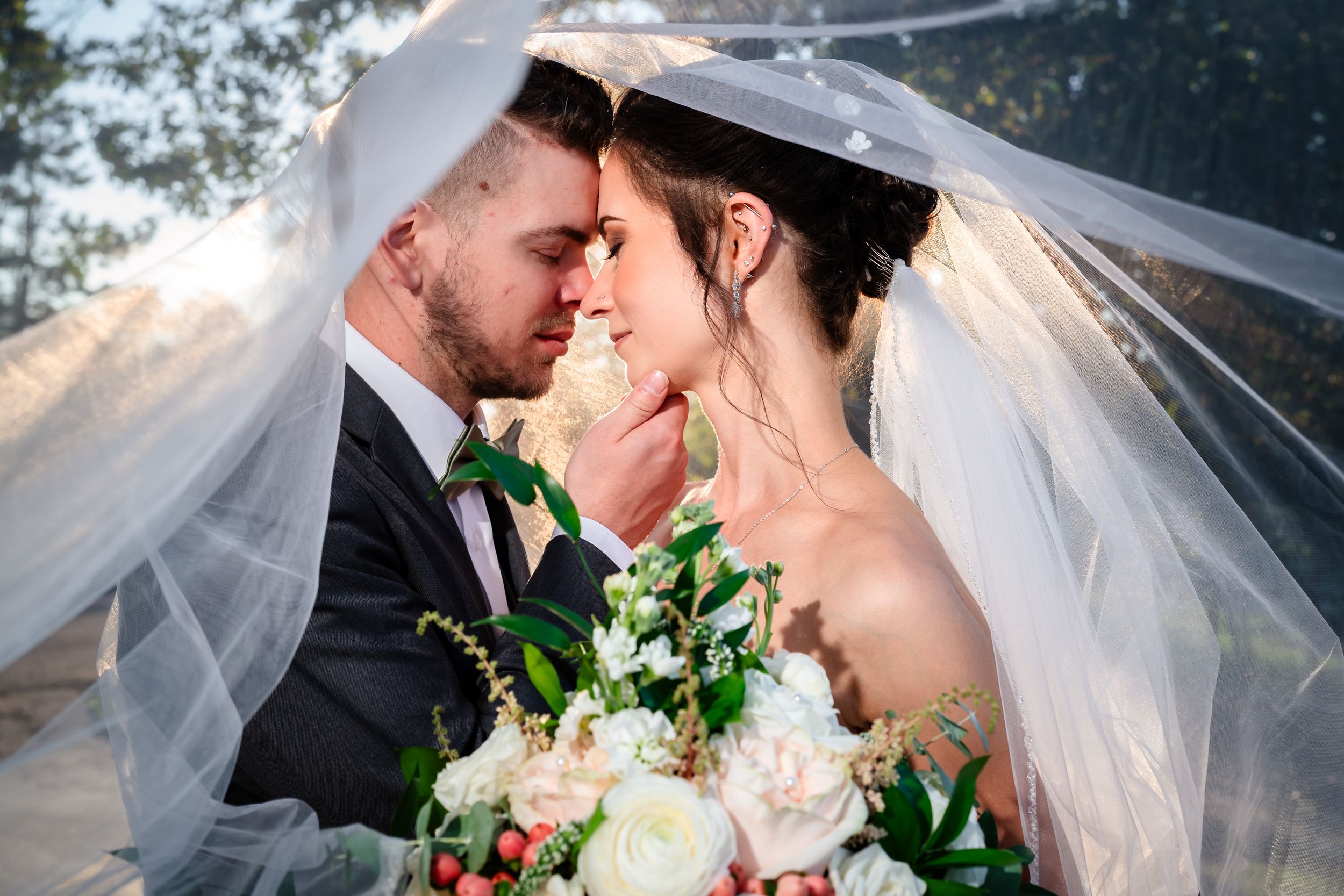 Romantic wedding couple sharing an intimate moment under a flowing white veil during their outdoor ceremony.