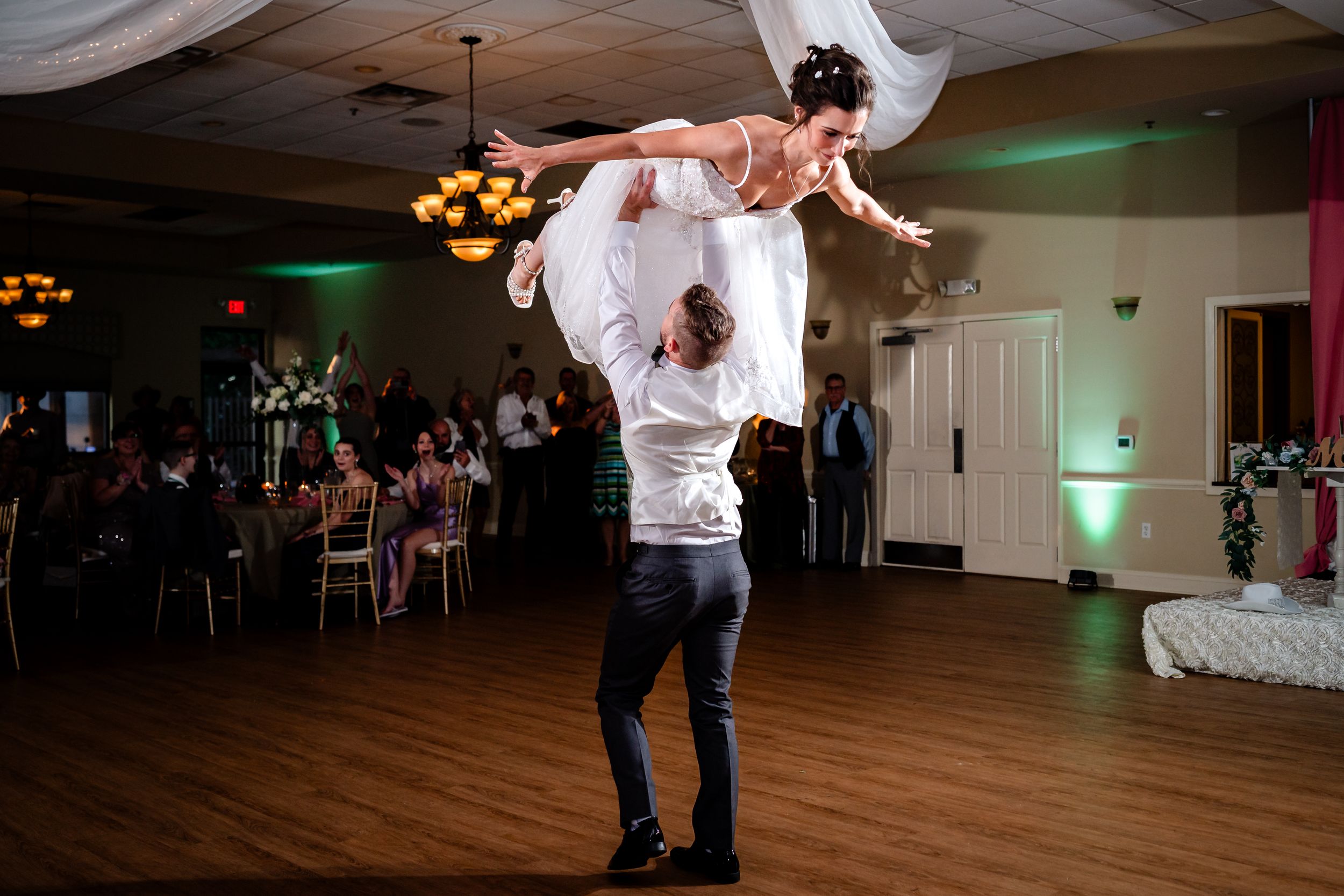 A couple performs a dance lift during a wedding reception in a ballroom with green accent lighting.