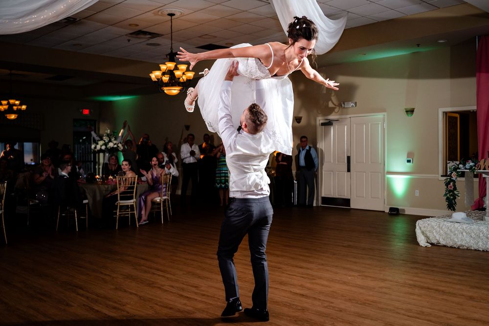 A couple performs a dance lift during a wedding reception in a ballroom with green accent lighting.