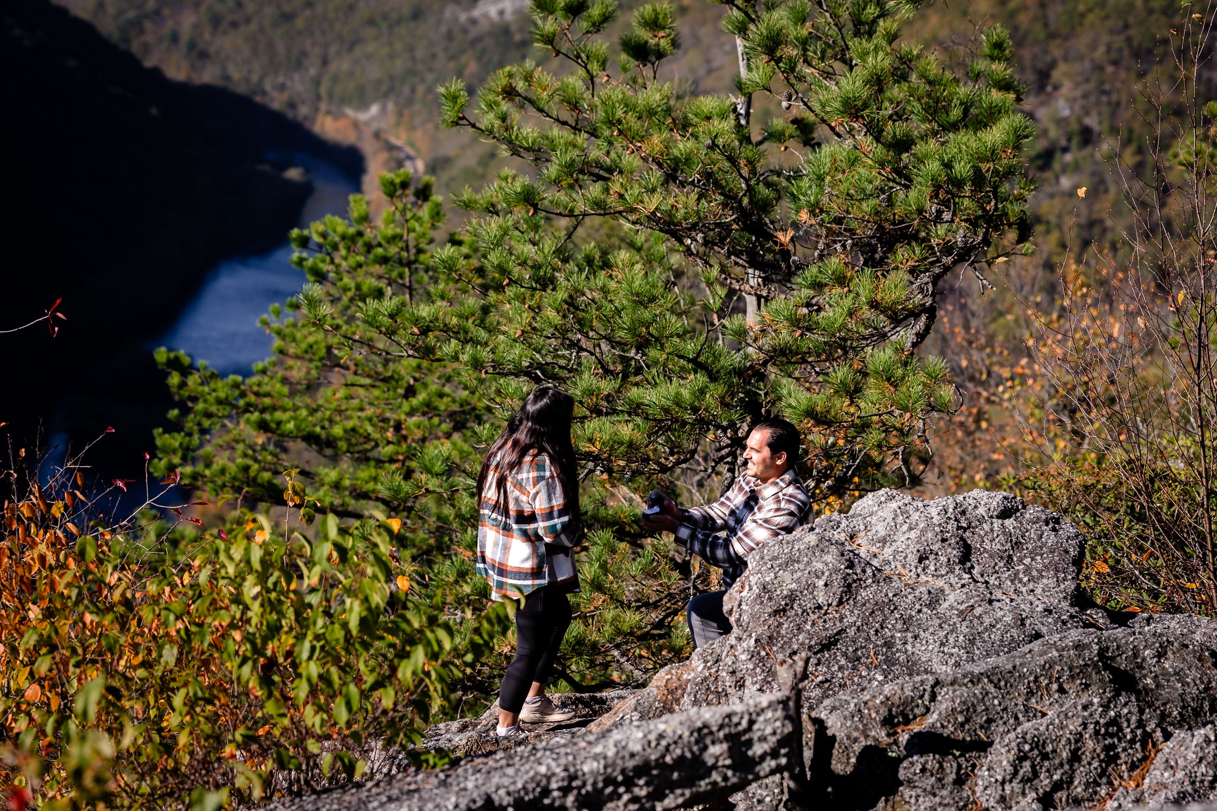 A scenic mountain trail winds through rocky terrain with hikers visible in the distance against a backdrop of autumn foliage.