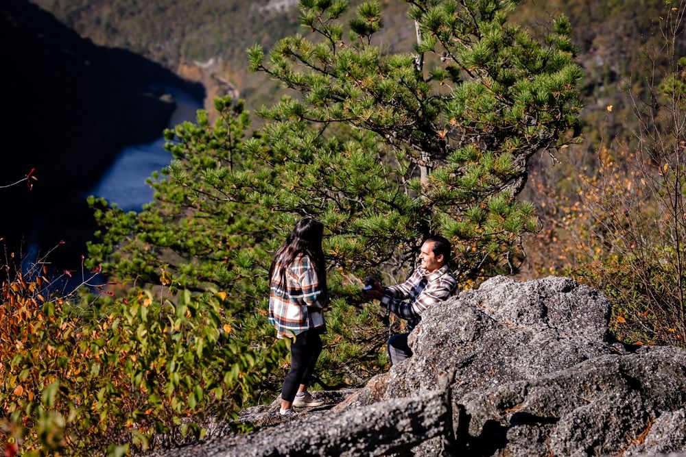A scenic mountain trail winds through rocky terrain with hikers visible in the distance against a backdrop of autumn foliage.