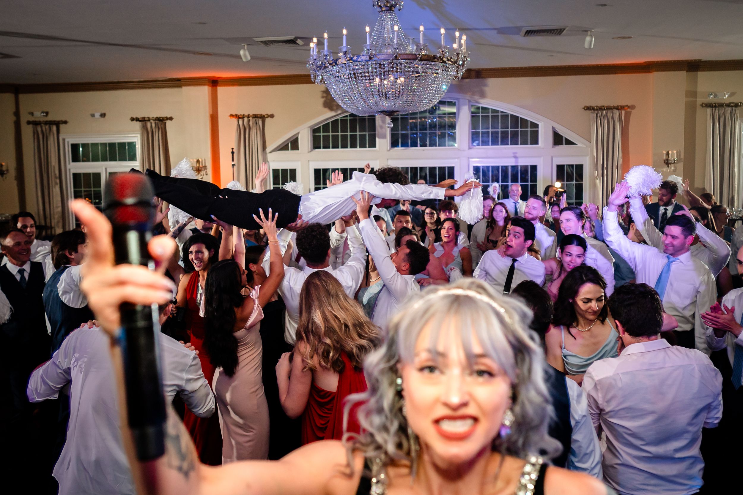 Wedding reception guests dancing and celebrating under crystal chandeliers in an elegant ballroom.