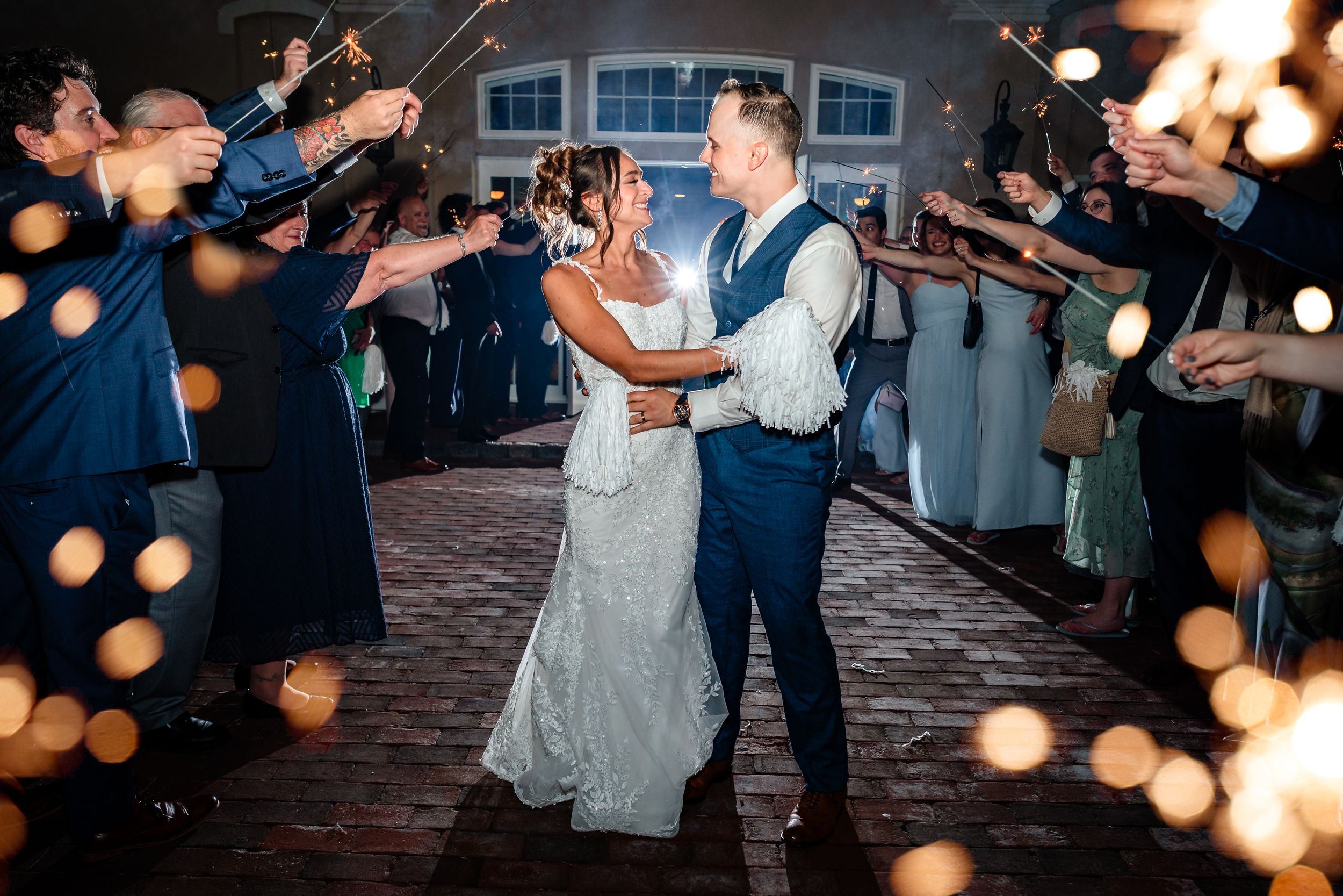 Couples dance together under romantic string lights at an evening wedding reception celebration.