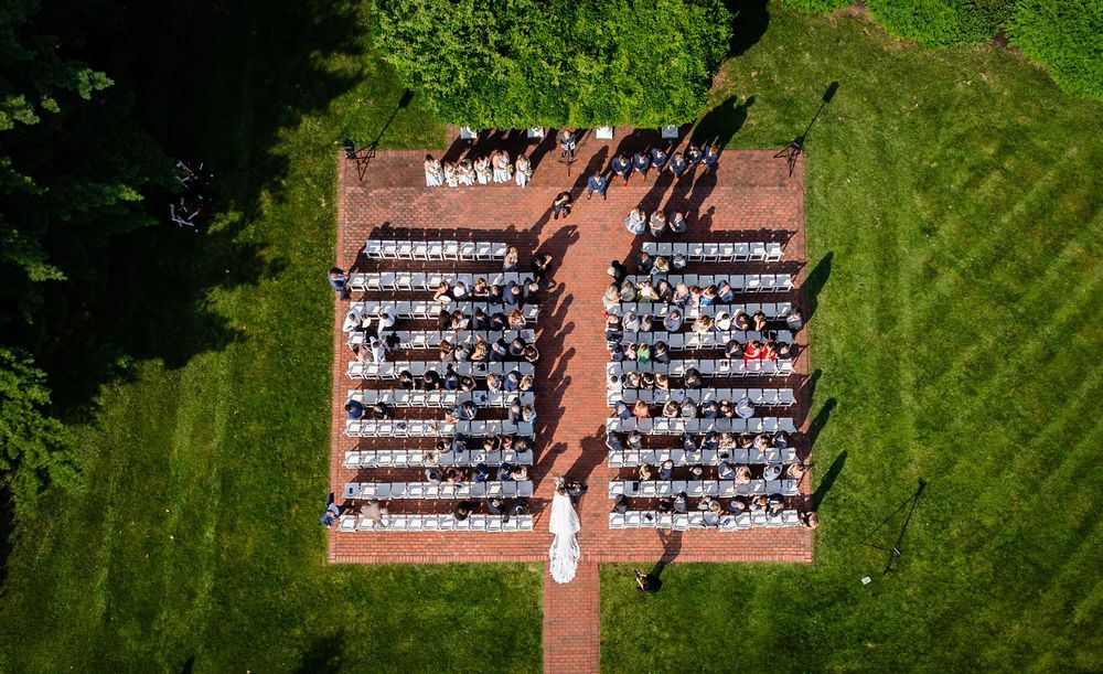 Aerial view of outdoor graduation ceremony with rows of white chairs arranged on green lawn and brick pathway.