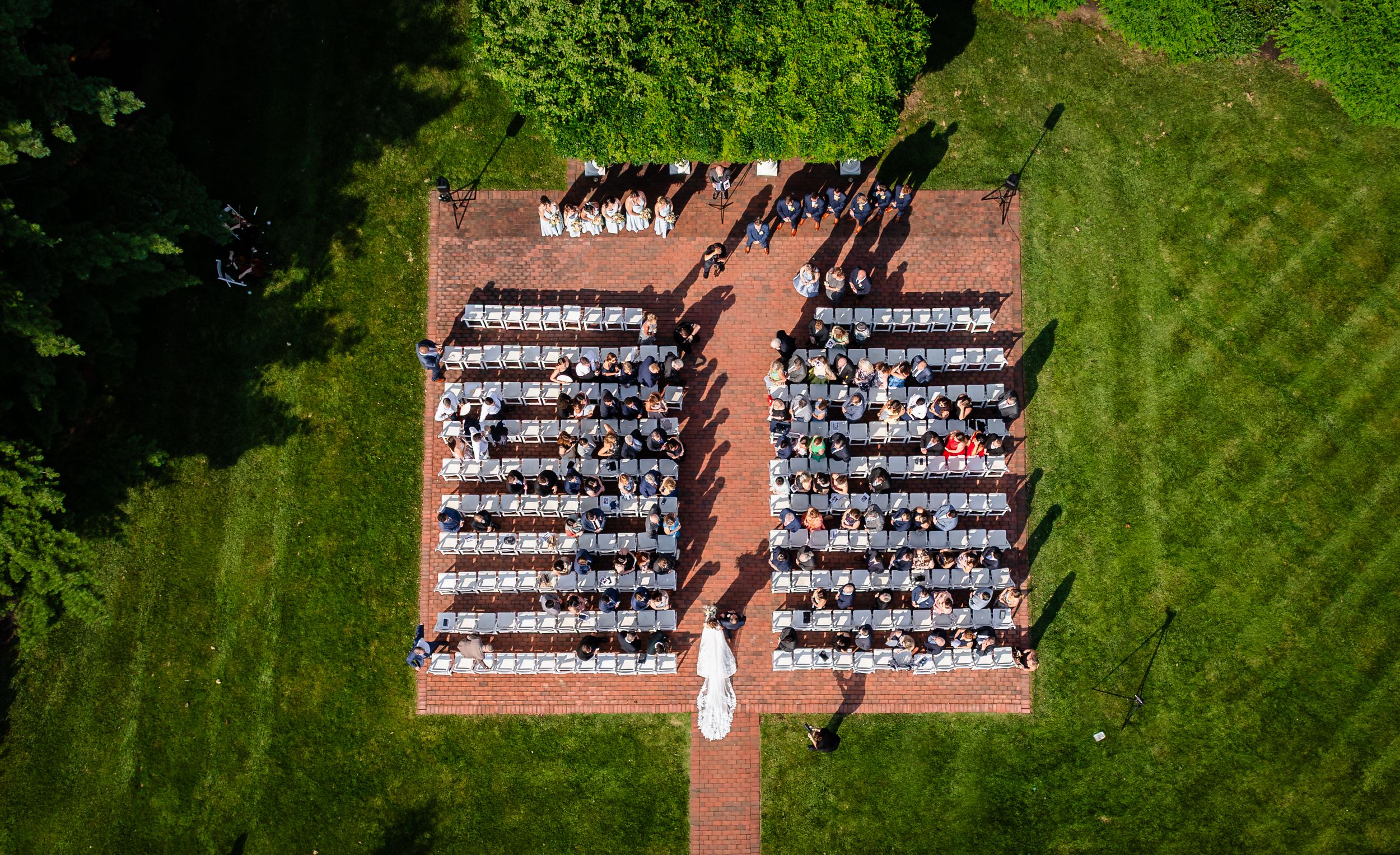 Aerial view of outdoor graduation ceremony with rows of white chairs arranged on green lawn and brick pathway.