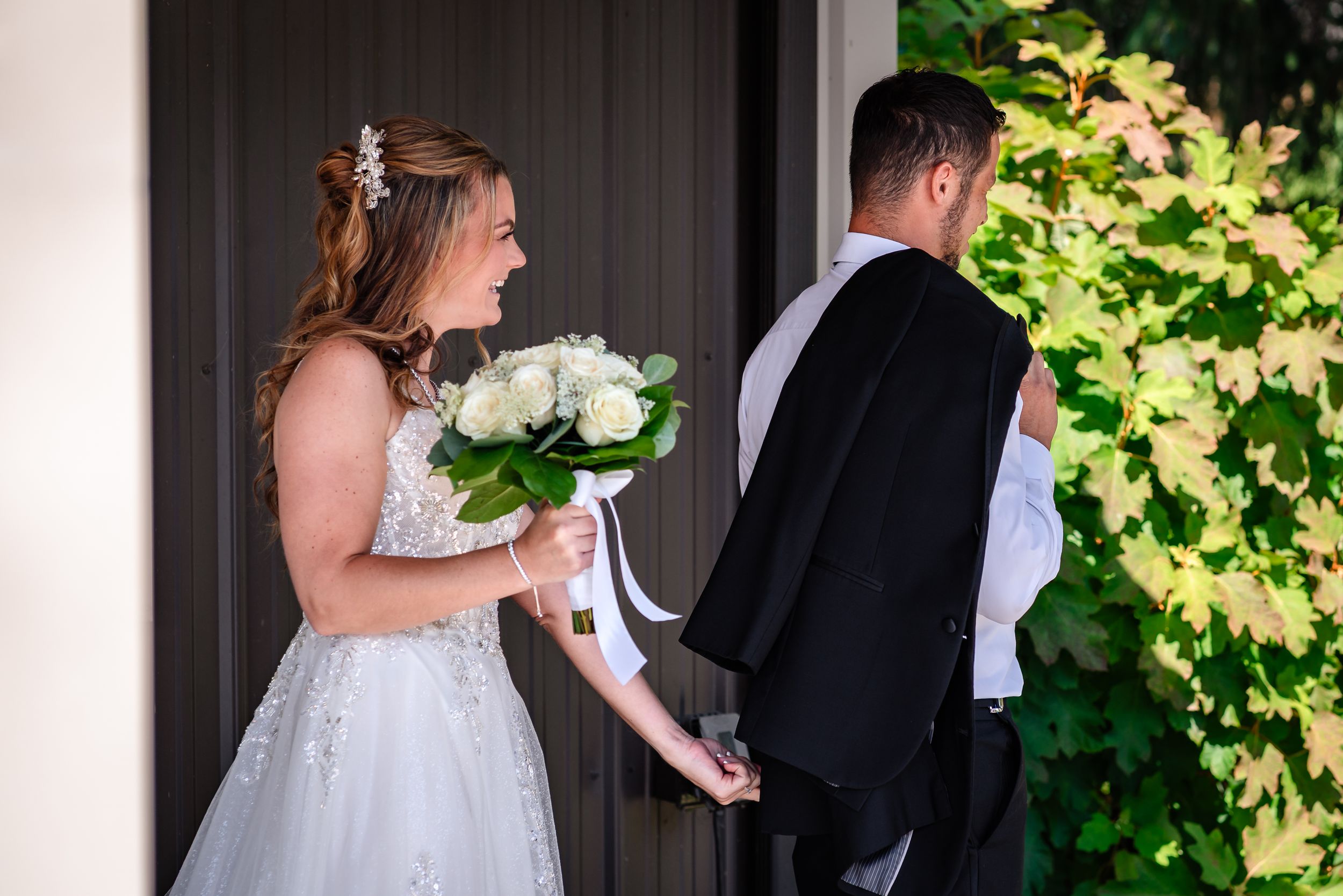 A bride and groom share a tender moment in front of a green vine-covered wall during their wedding ceremony.