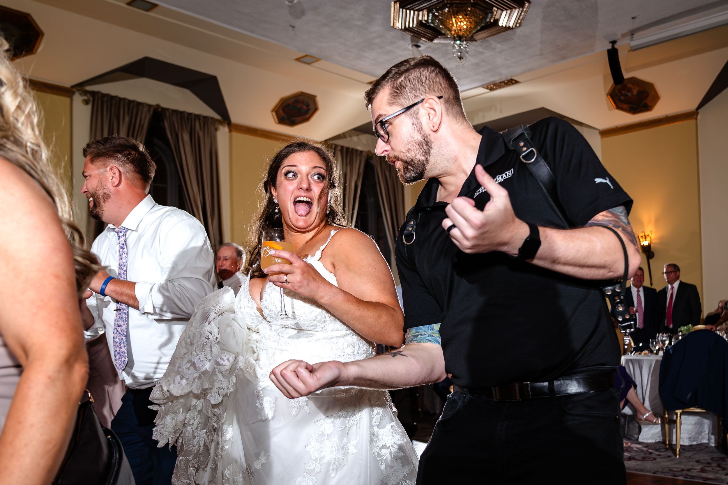 Wedding guests dance and celebrate together on a dimly lit dance floor during a reception party.