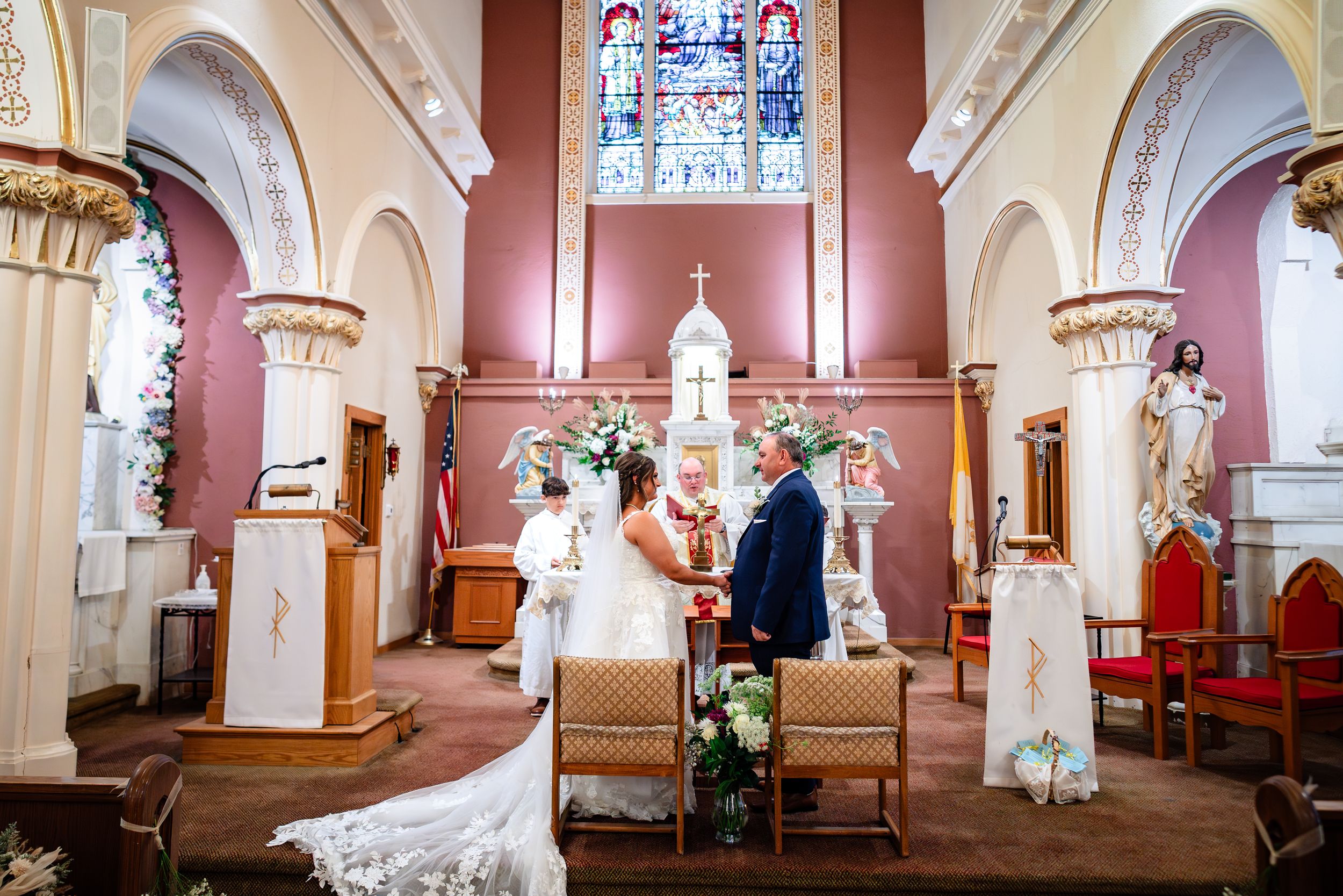 A panoramic view of a church interior with stained glass windows, ornate columns, and white arches in traditional design.