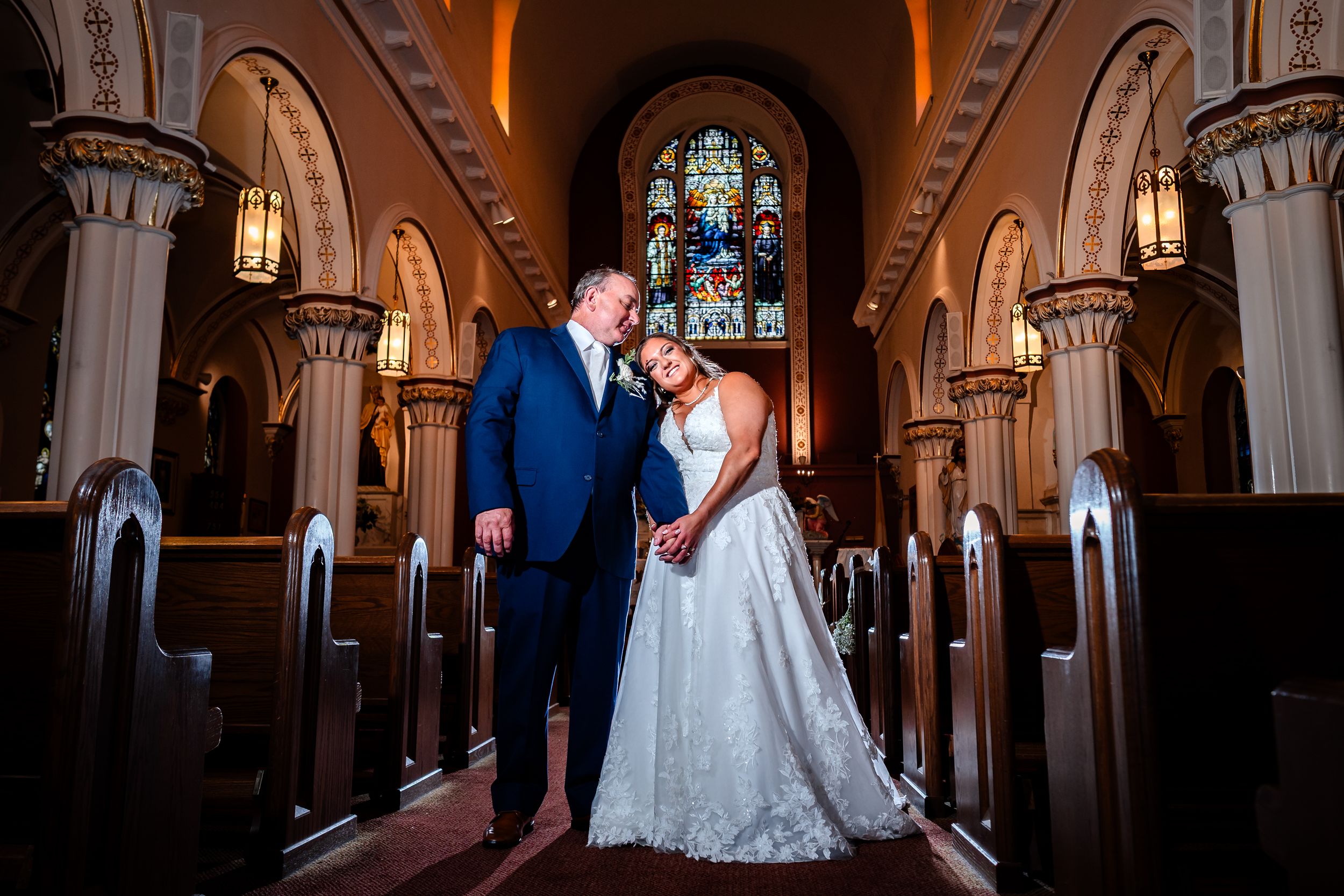 A couple shares a romantic dance in an elegant church venue with stained glass windows and arched architecture.