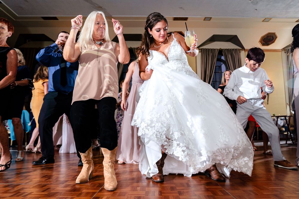 Wedding guests dance and celebrate on a wooden dance floor at a reception venue.