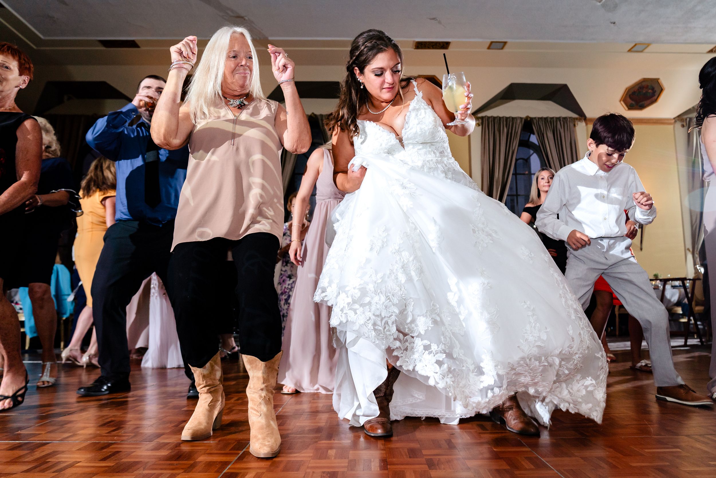 Wedding guests dance and celebrate on a wooden dance floor at a reception venue.