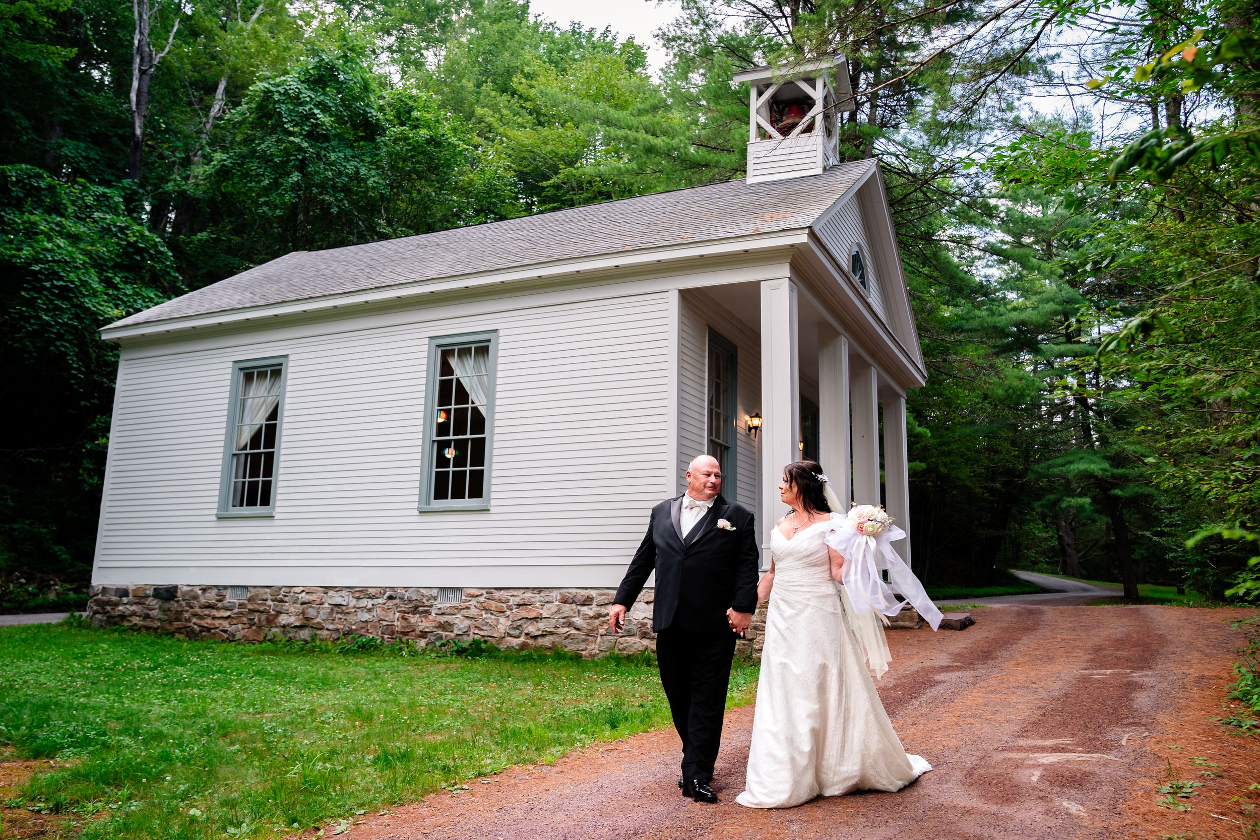 A small white chapel nestled among lush green trees creates a serene wedding ceremony setting.