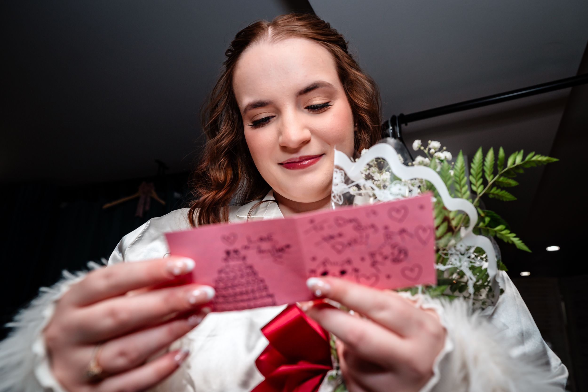 Someone holds and reads a burgundy colored ticket or card while smiling in a dimly lit setting.