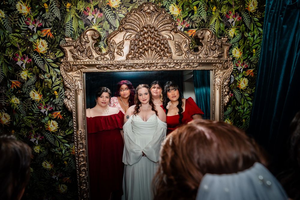 A group of people posing together in formal attire against an ornate backdrop with greenery and golden decor.