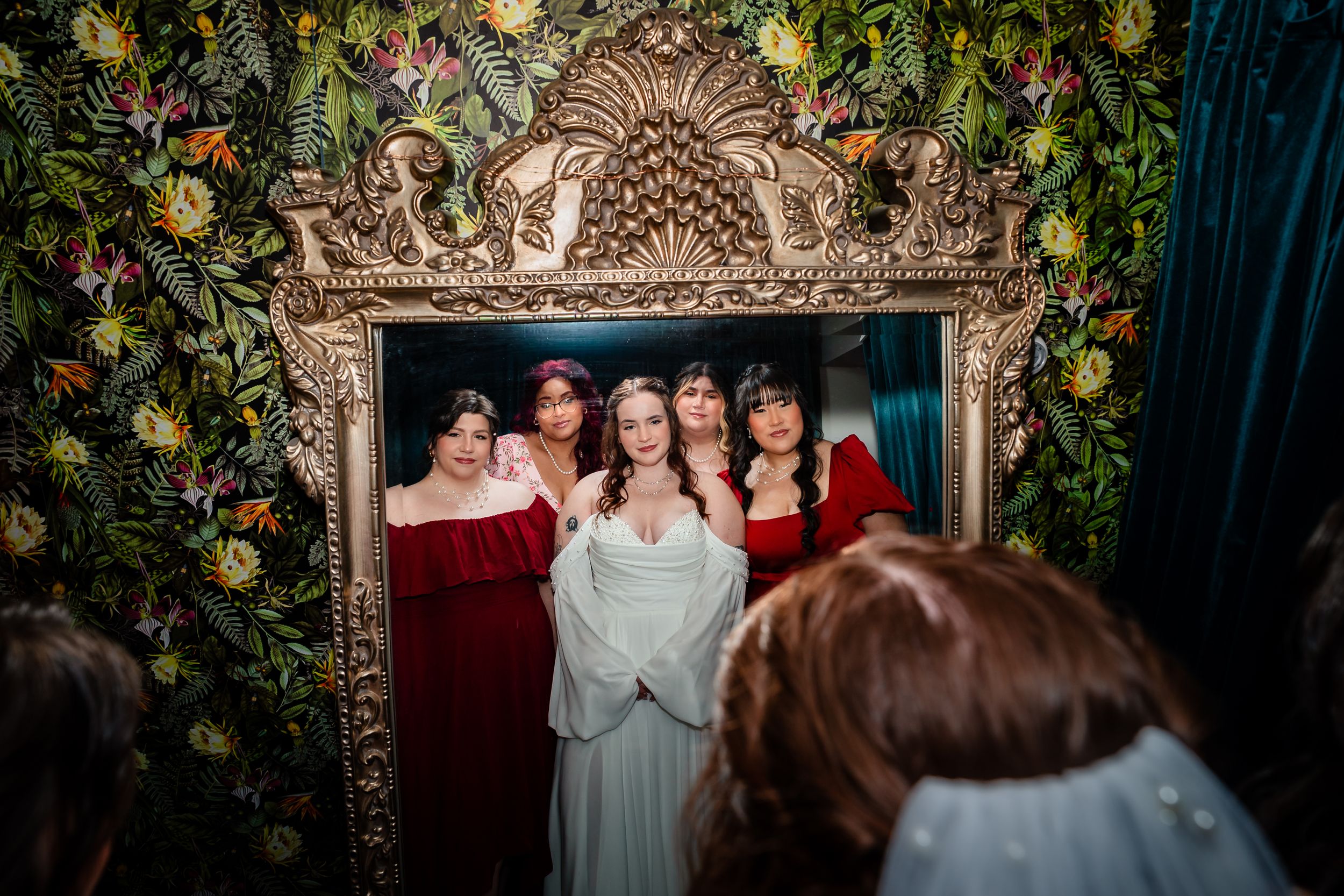 A group of people posing together in formal attire against an ornate backdrop with greenery and golden decor.