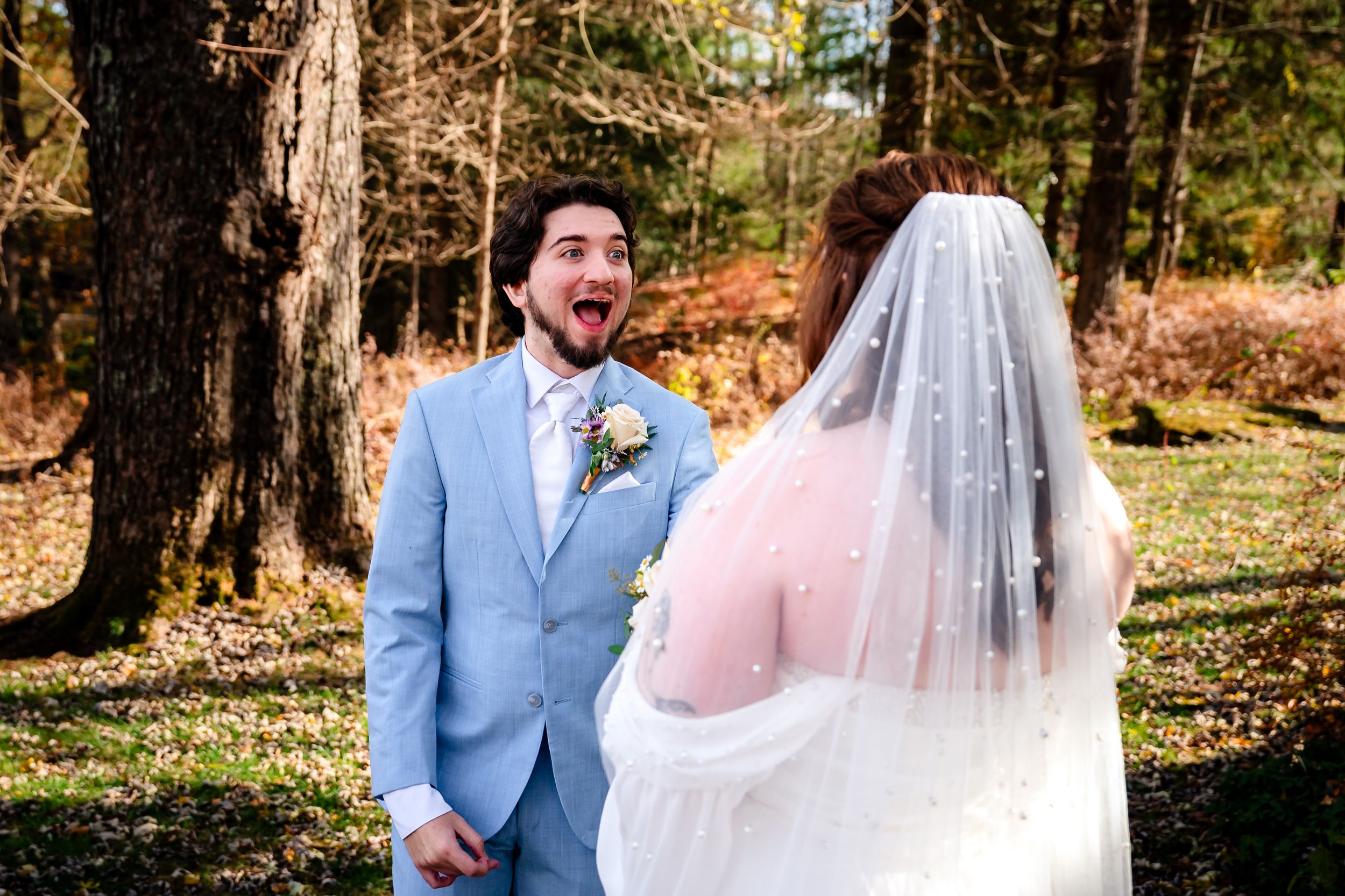 A couple shares an intimate moment in a wooded outdoor setting during an autumn wedding ceremony.